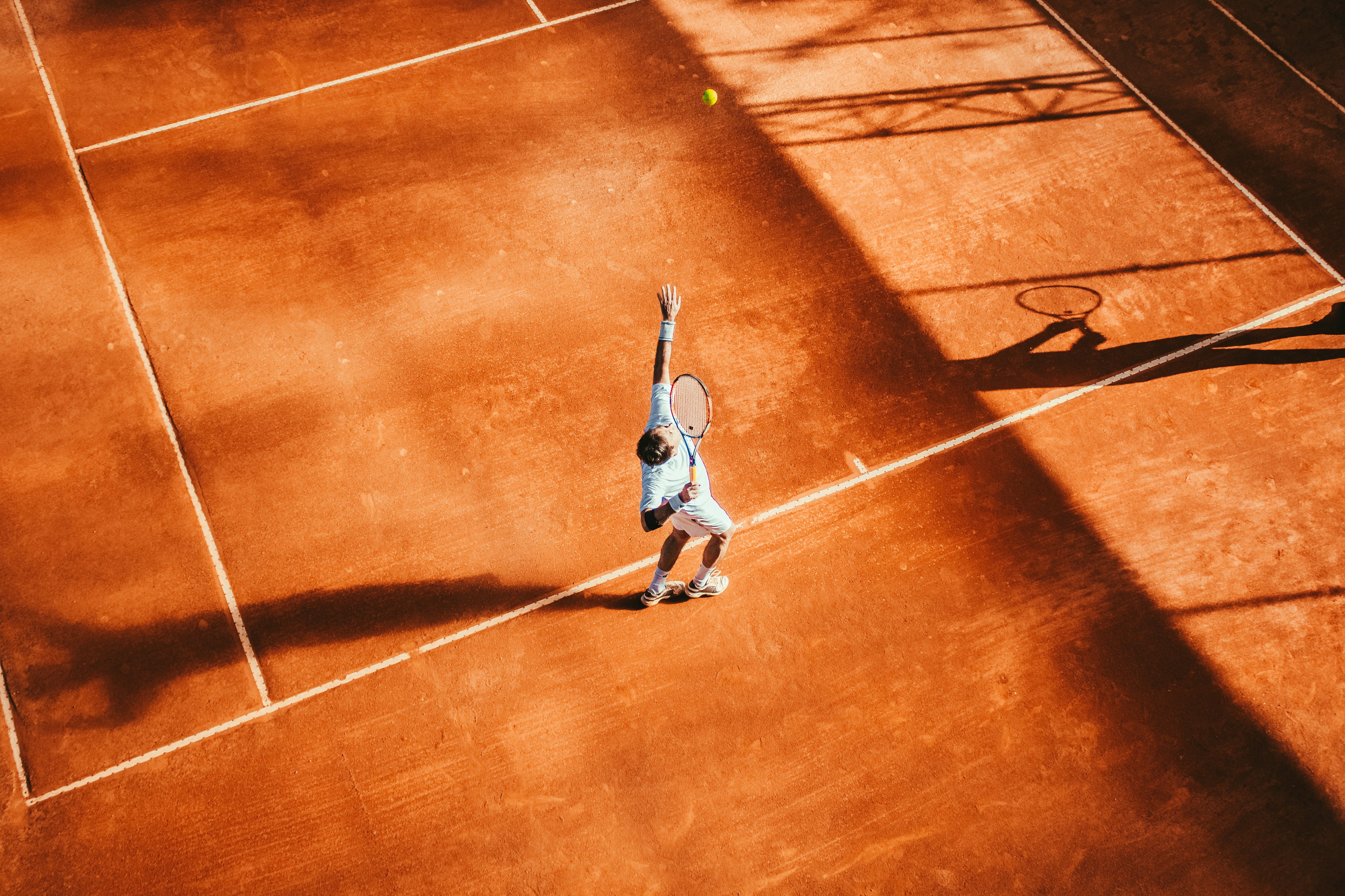 A tennis player reaching for the ball in a reused photograph on a clay court